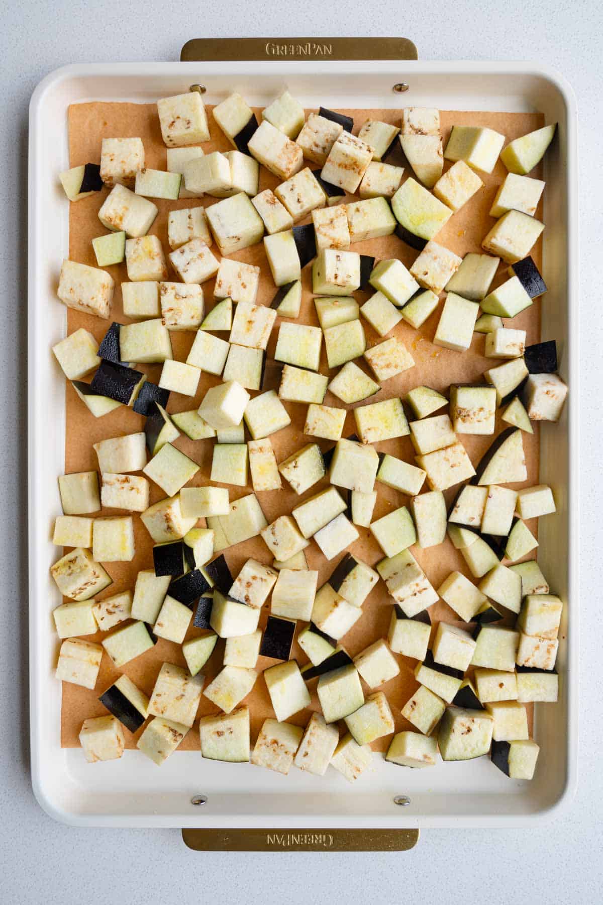 Cubed eggplant on a parchment-lined baking sheet.