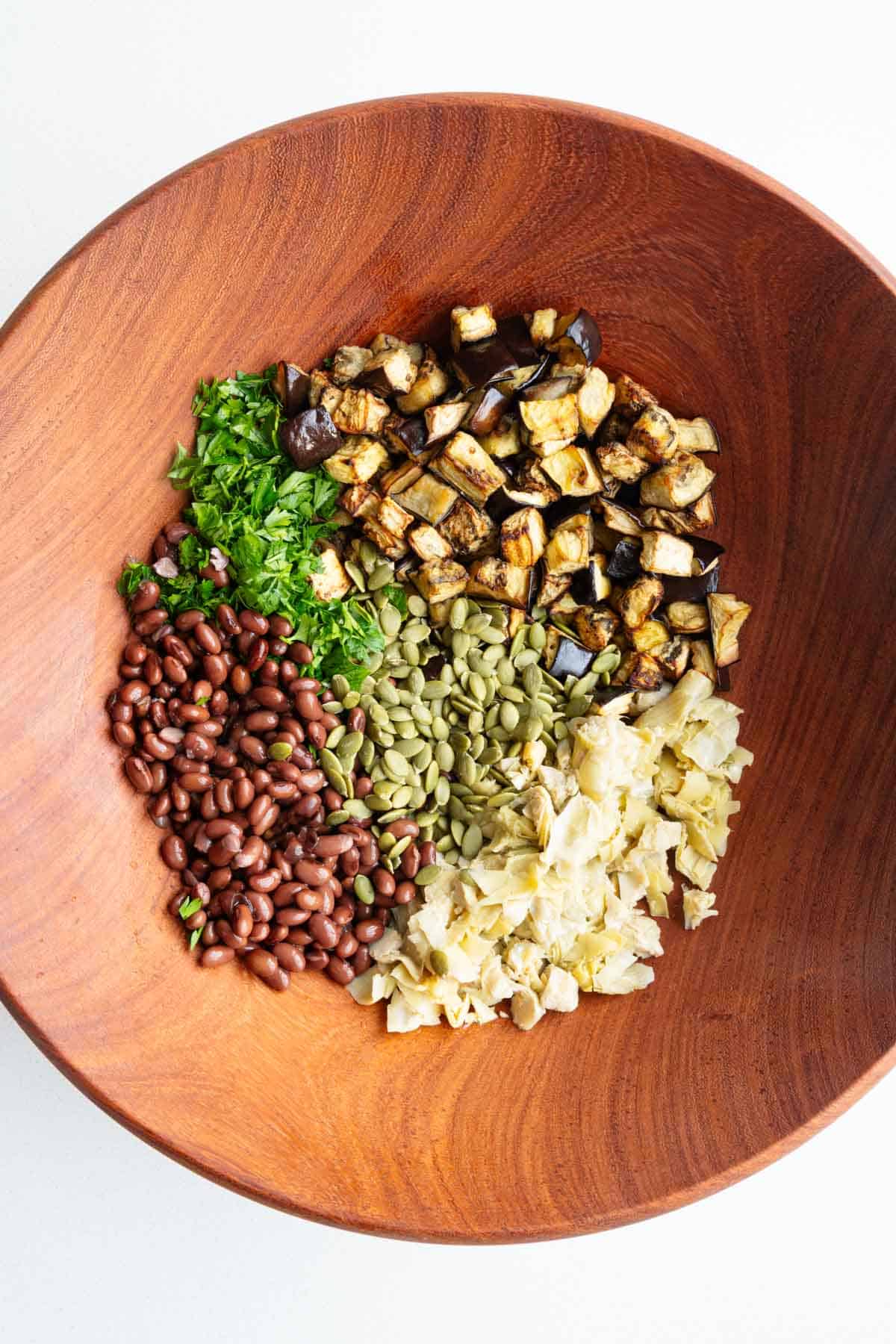 Eggplant, beans, artichoke hearts, pumpkin seeds, and parley in a bowl.