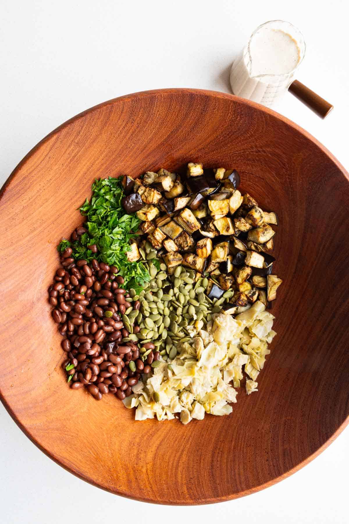 Eggplant, beans, artichoke hearts, pumpkin seeds, and parley in a large bowl.
