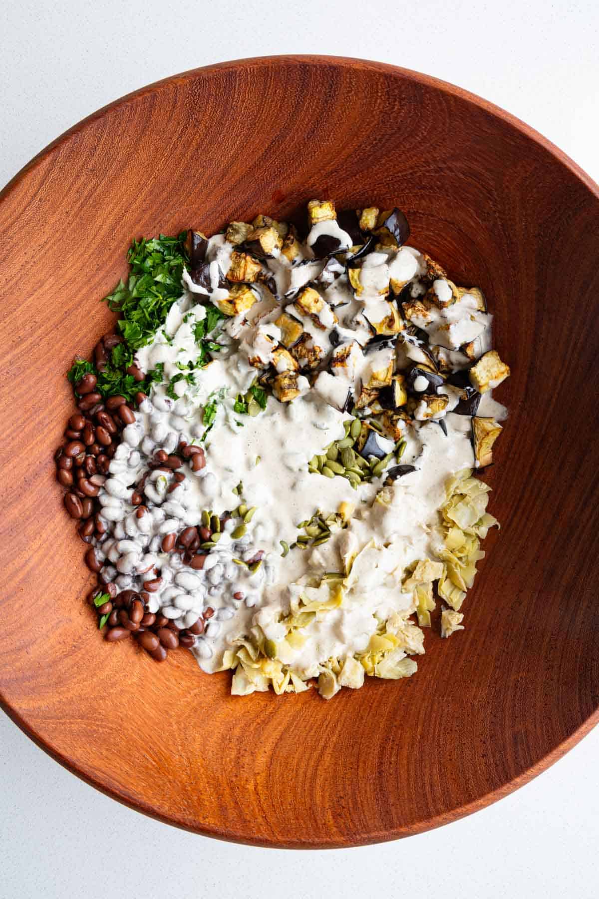 Eggplant, beans, artichoke hearts, pumpkin seeds, and parley in a large bowl with pickle juice dressing.