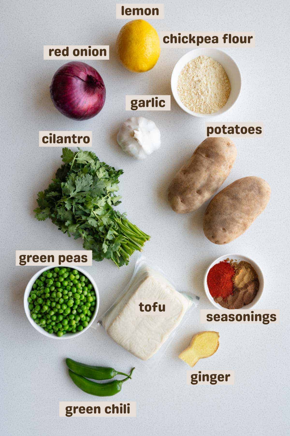Tofu, potatoes, green chilis, ginger, garlic, green peas, lemon, seasonings, chickpea flour, and cilantro.