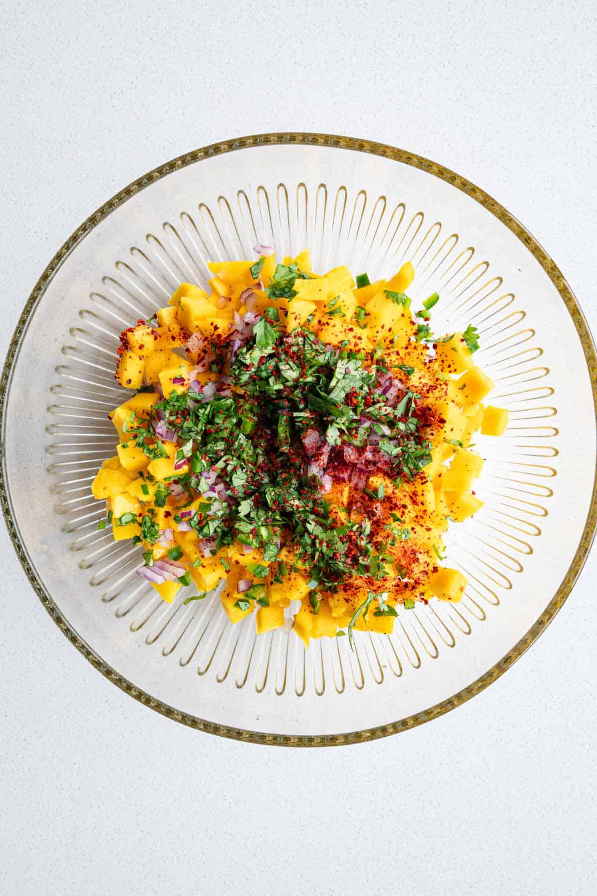Chopped mango, red onion, jalapeño, lime juice, red pepper powder, and cilantro in a bowl.