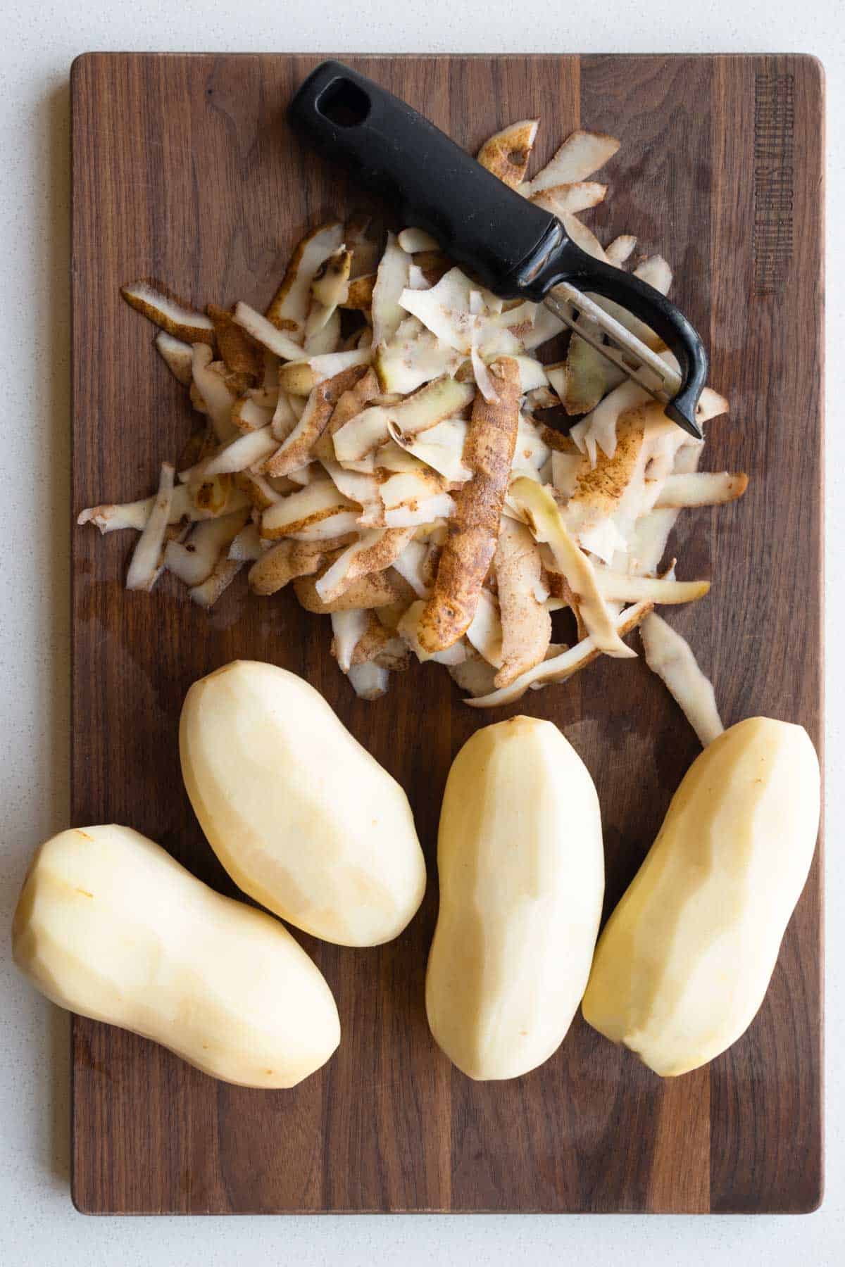 Peeled potatoes on a cutting board with a peeler.
