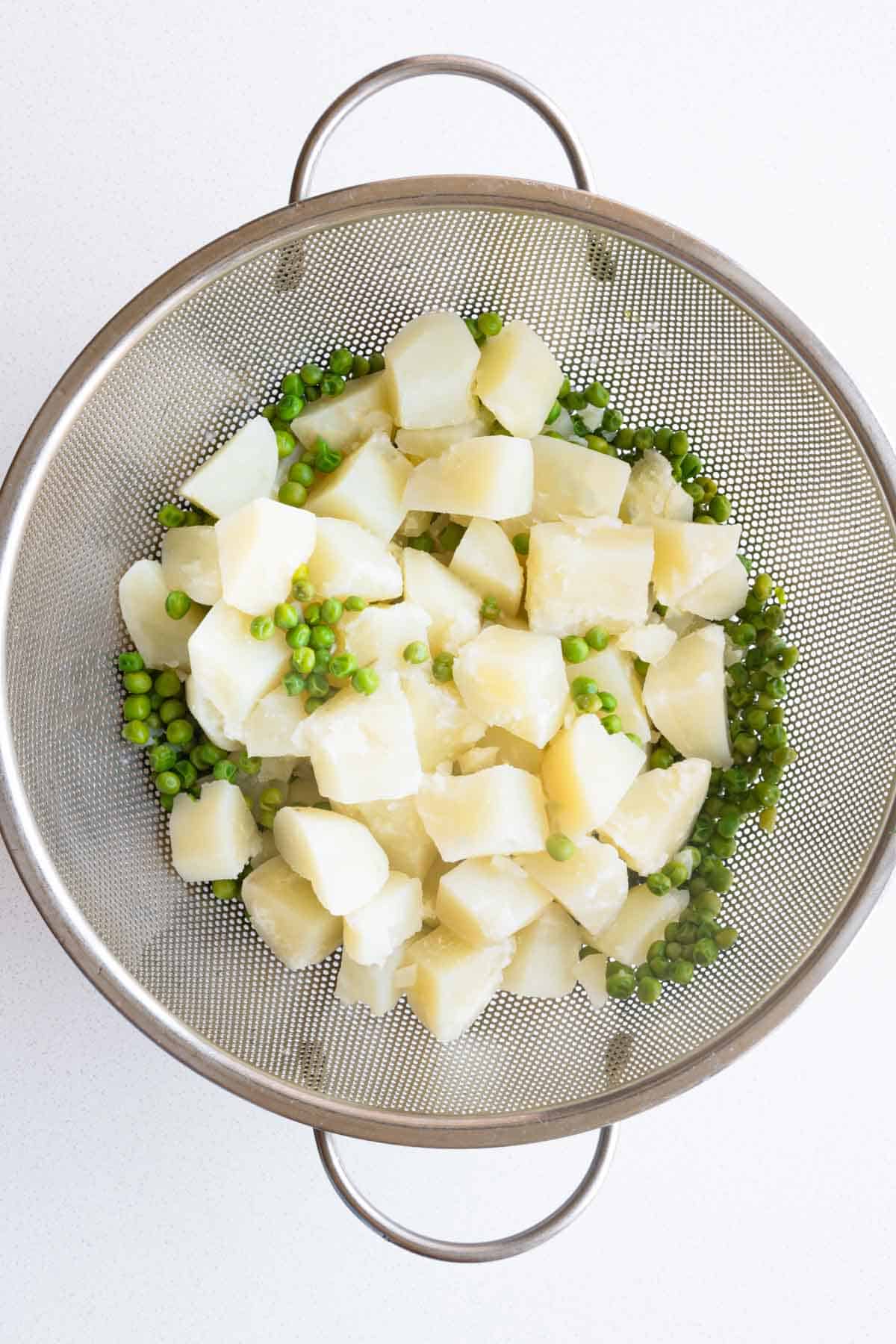 Cut cooked potatoes and green peas in a large mesh colander.