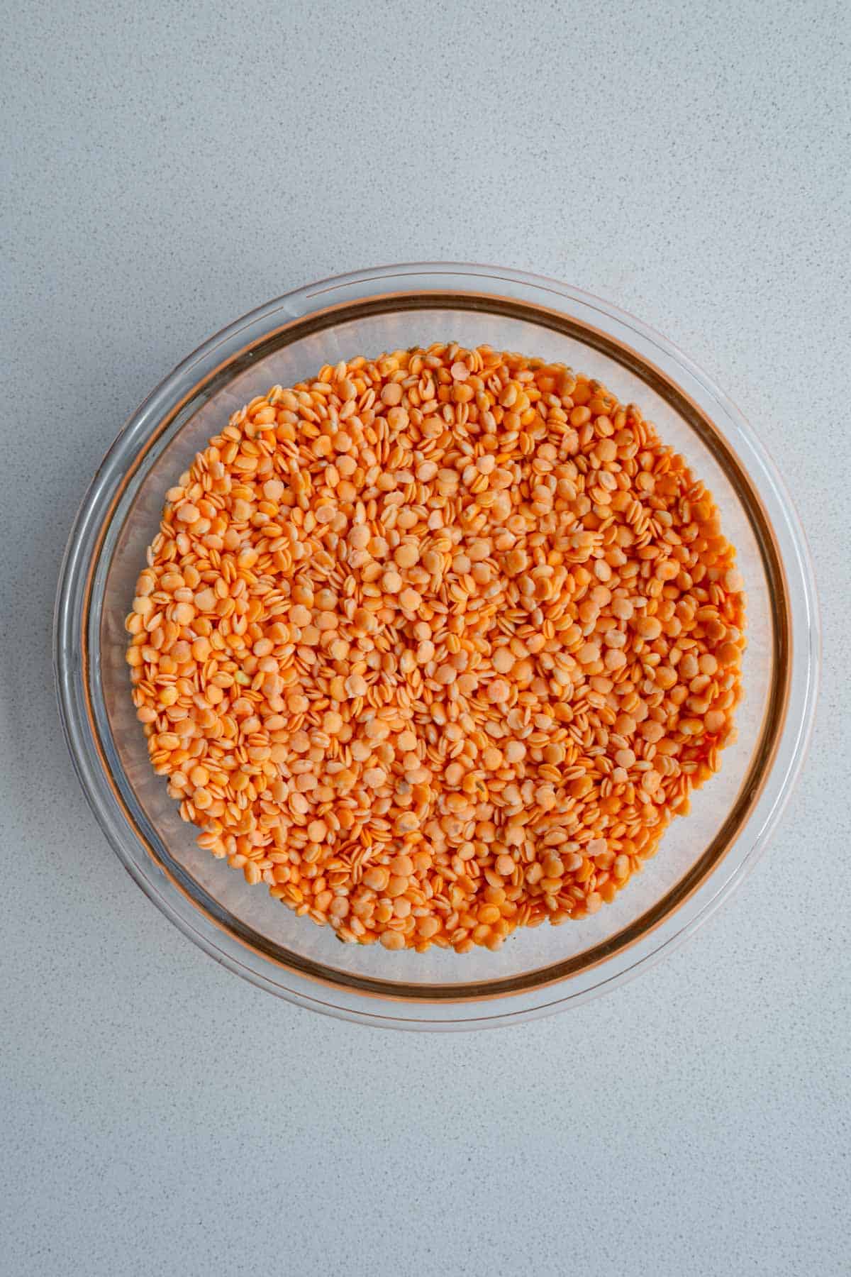 Red lentils soaking in water in a glass bowl.