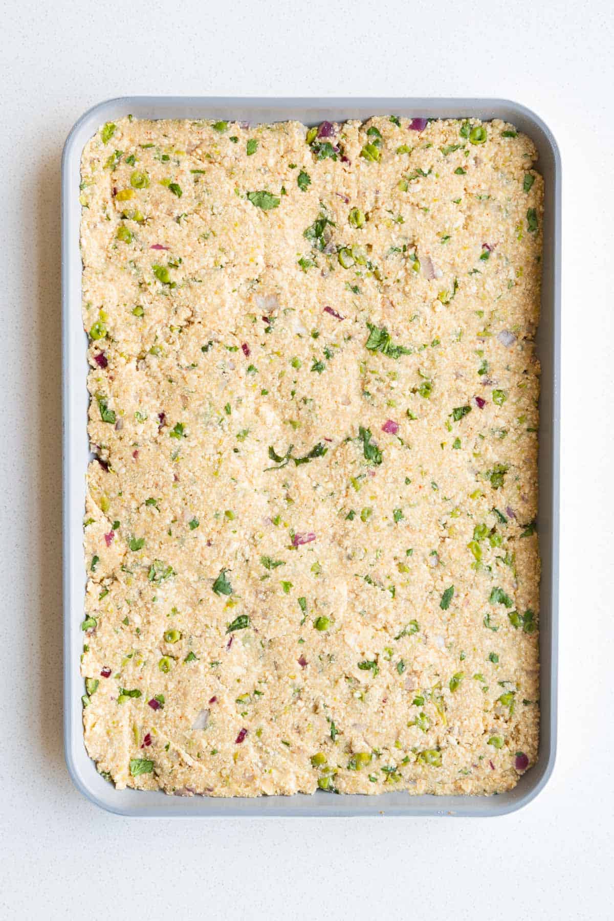 Mashed tofu, potatoes, chickpea flour and vegetables pressed into a sheet pan.