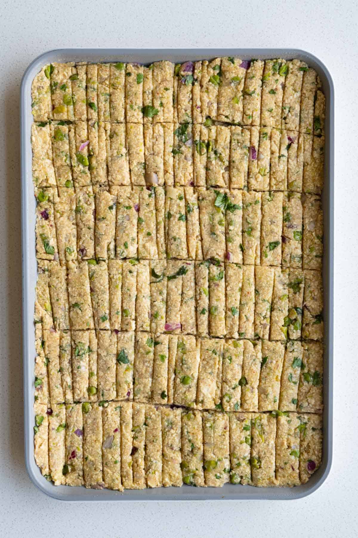 Mashed tofu, potatoes, chickpea flour and vegetables pressed into a sheet pan, scored into kebab-shaped portions before baking.