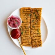 Sheet-pan vegan kebabs on a white plate with ketchup and pickled red onion.