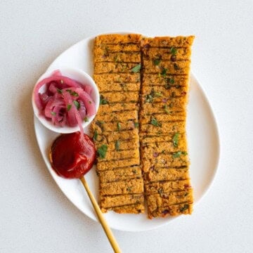Sheet-pan vegan kebabs on a white plate with ketchup and pickled red onion.