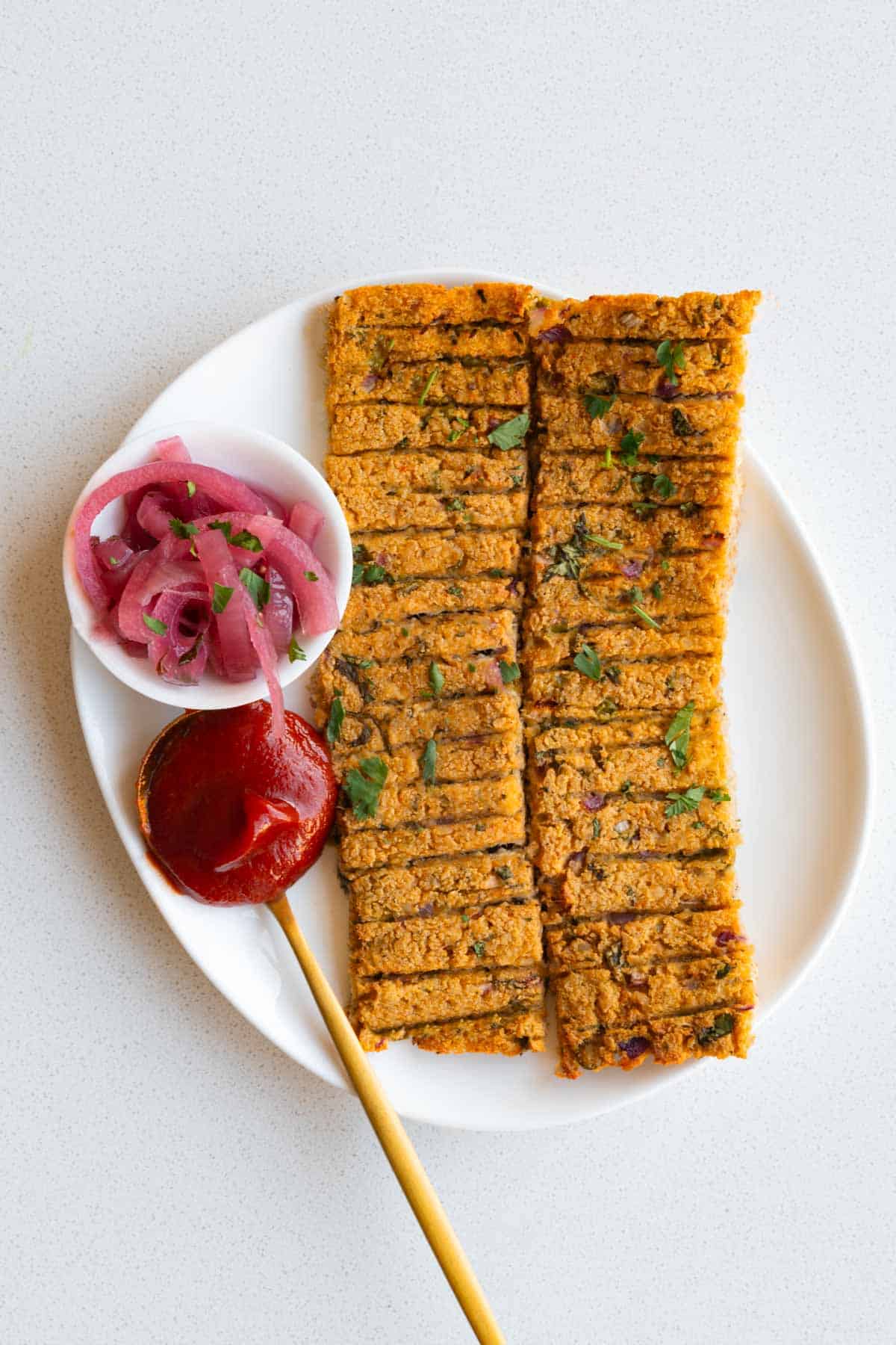 Sheet-pan vegan kebabs on a white plate with ketchup and pickled red onion.