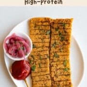 Sheet-pan vegan kebabs on a white plate with ketchup and pickled red onion.