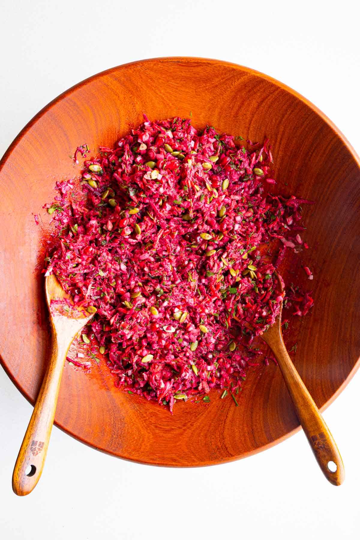 Beetroot Salad with Pomegranate, carrots, fresh herbs, onion, pumpkin seeds, and tahini dressing in a wooden bowl.