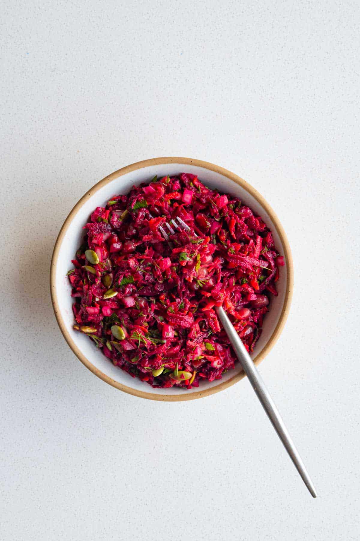 Beetroot salad with pomegranate in a bowl with a fork.