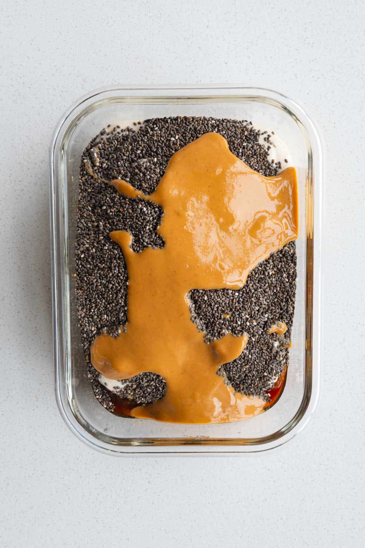 Mashed Medjool dates, water, chia seeds, yogurt, nut butter, and vanilla extract in a glass dish.