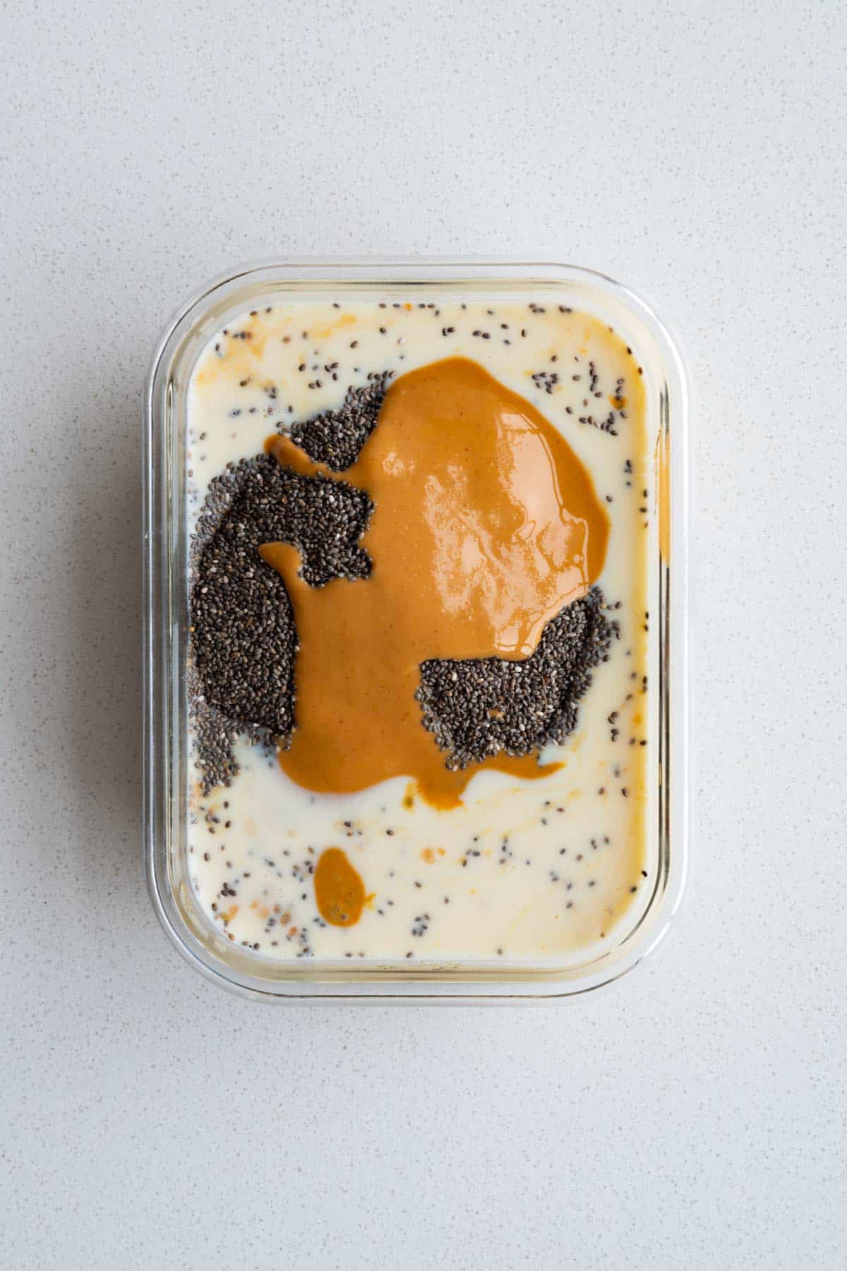 Mashed Medjool dates, chia seeds, yogurt, nut butter, nondairy milk, and vanilla extract in a glass dish.