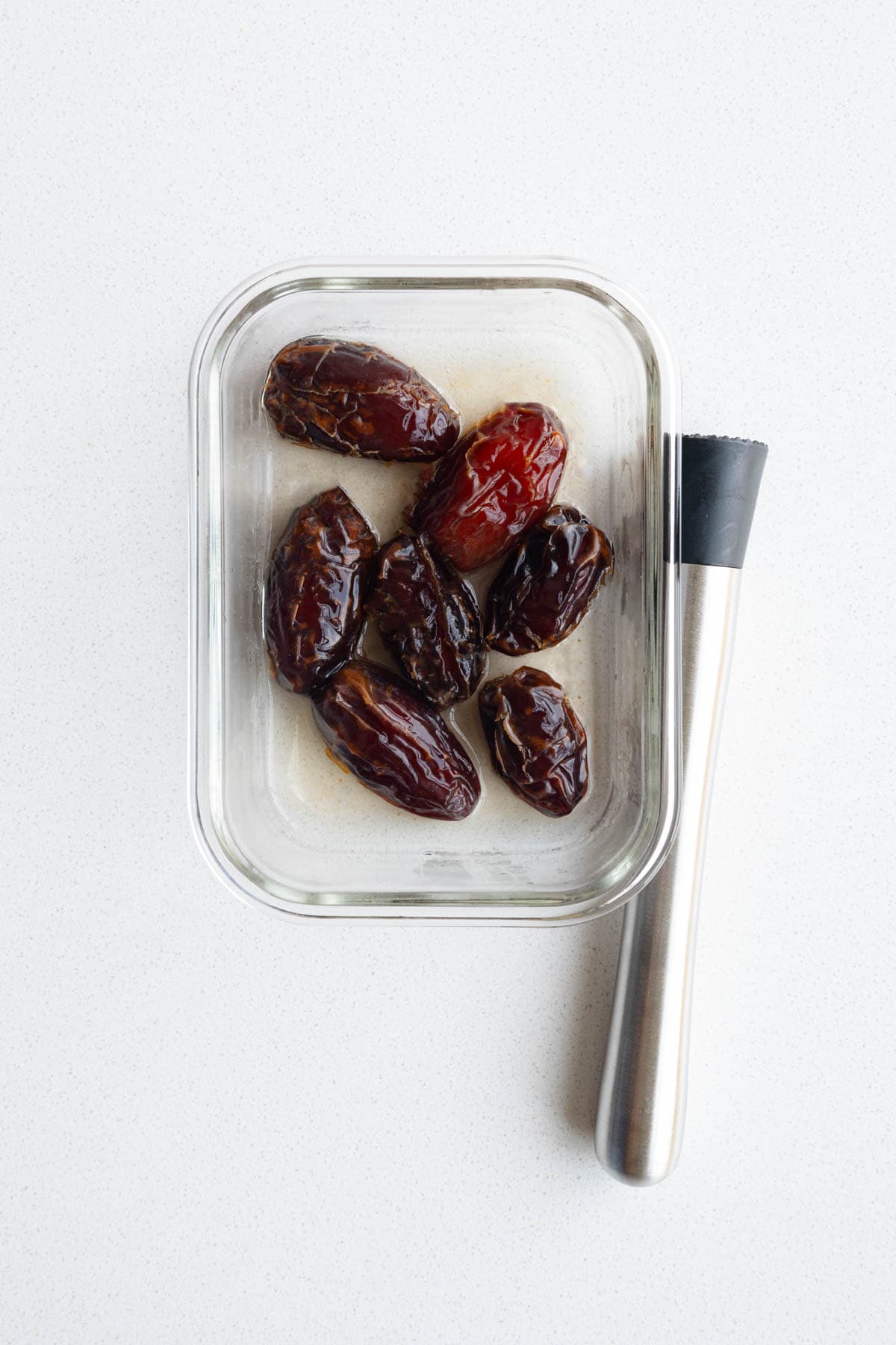 Medjool dates in water in a glass dish with a muddler.