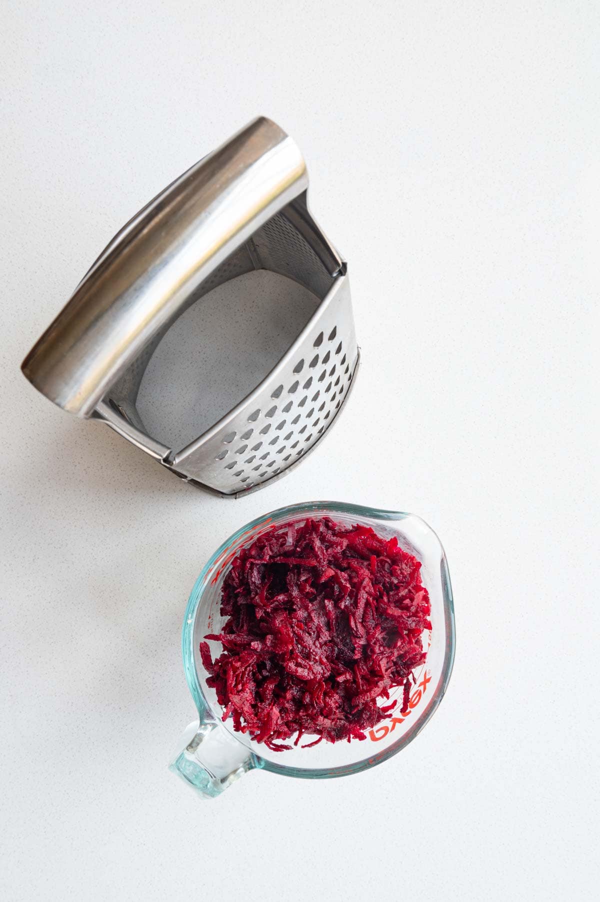 Grated beetroot in a measuring cup beside a box grater.
