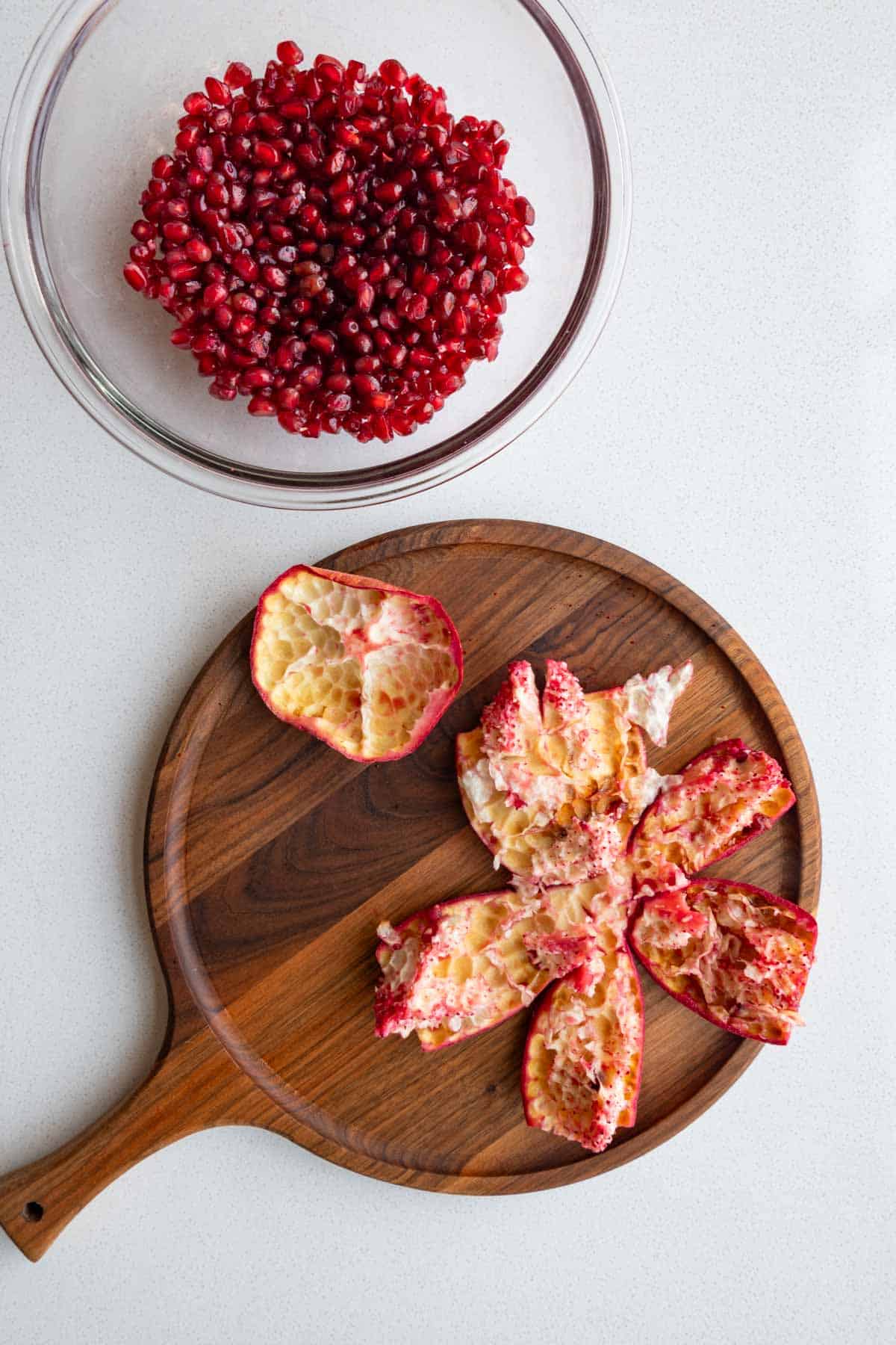 Pomegranate seeds in a bowl next to the skin.