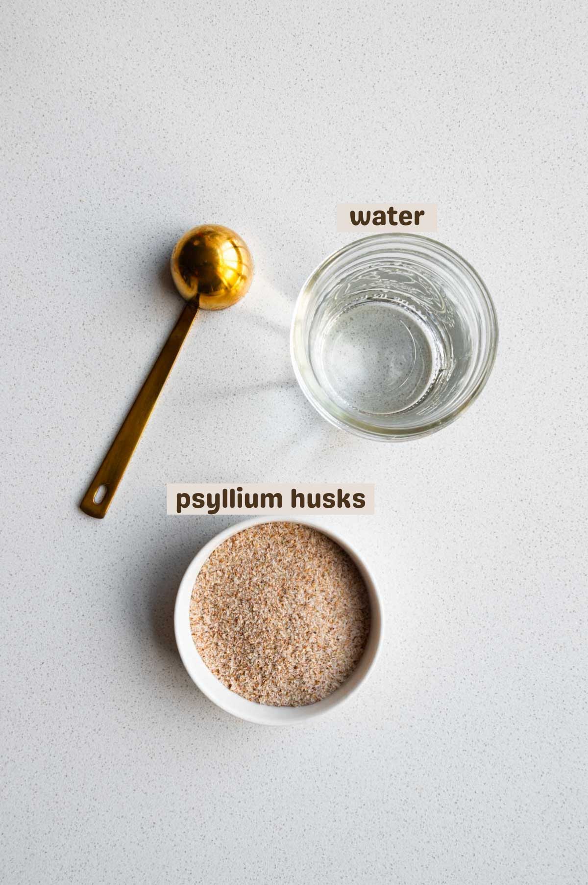 Whole psyllium husks, a glass of water, and a tablespoon.