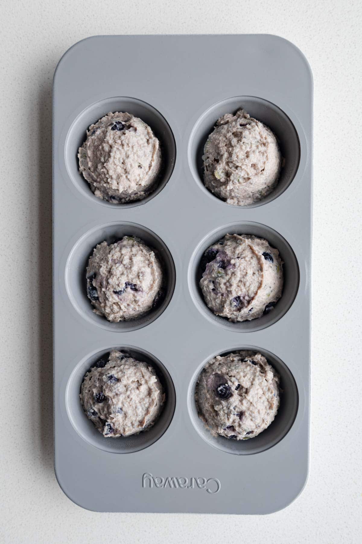Batter scooped into the holes of a muffin tin.