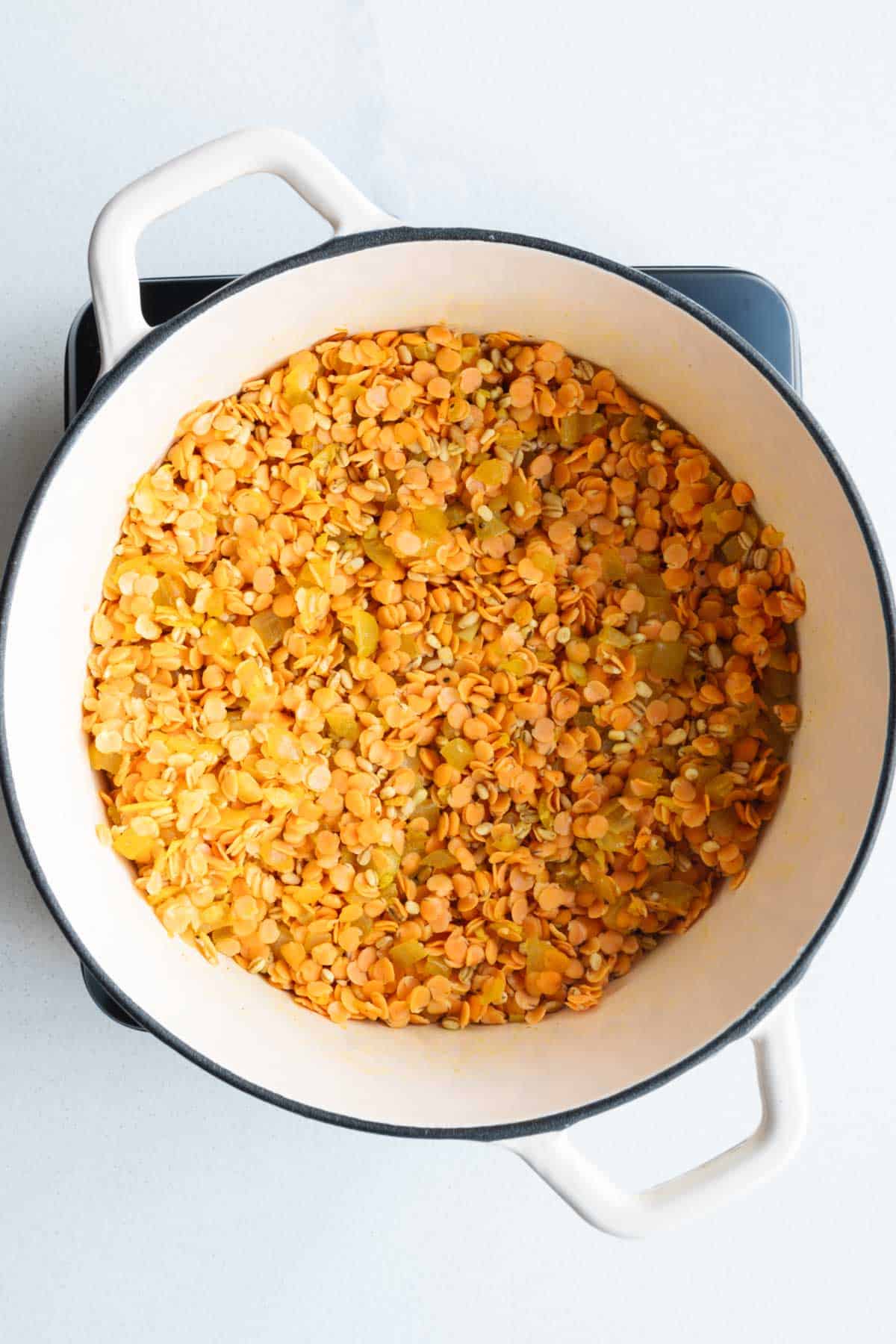 Dried red lentils, barley, cooked aromatics, and seasonings in a saucepan.