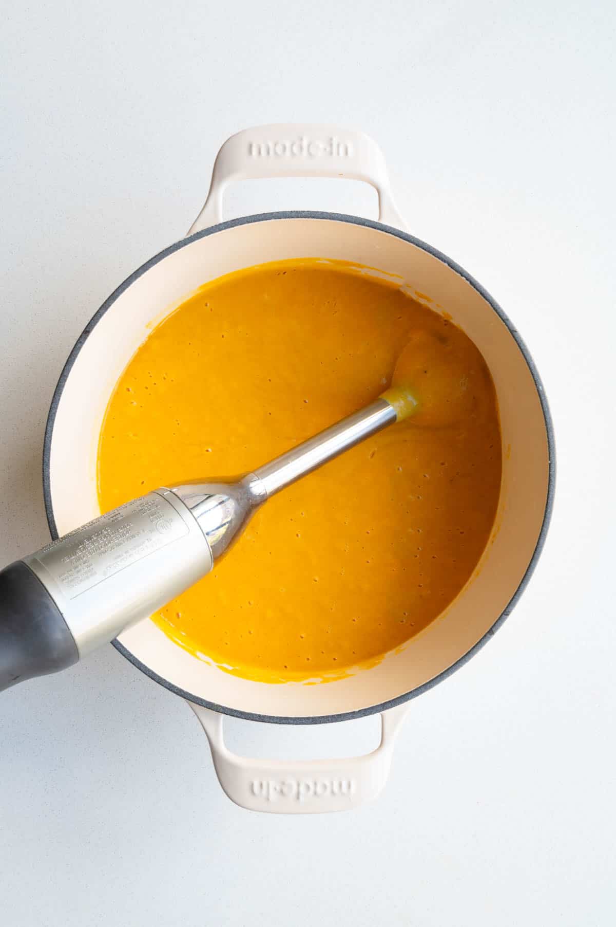 Blended red lentils, barley, seasoning, and carrots in a saucepan with an immersion blender.