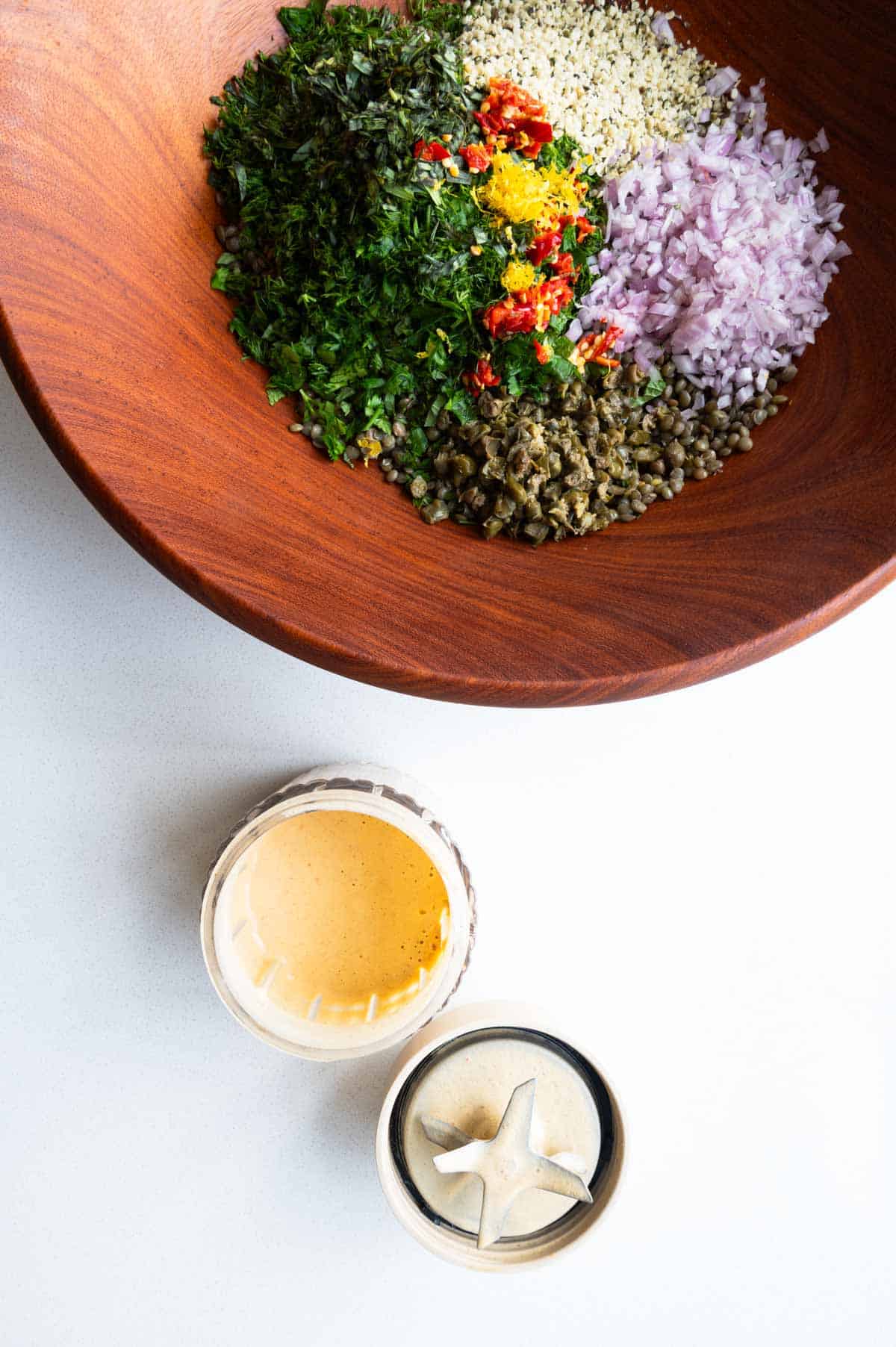 Lentils, chopped bell pepper, fresh herbs, shallots, capers, lemon zest, hemp hearts, Calabrian chilis, and red wine vinegar in a wooden bowl with tahini pickle juice dressing.