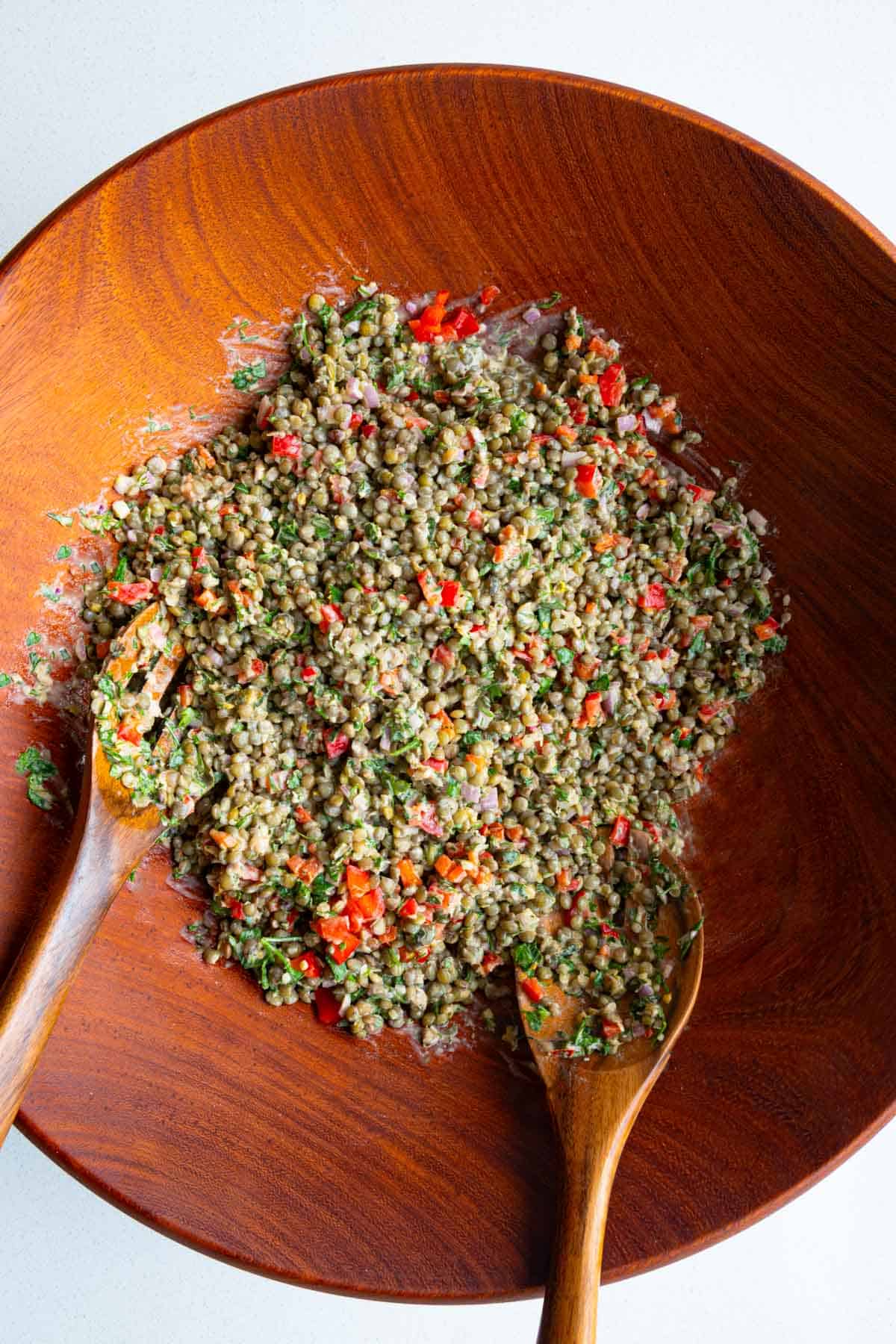 Lentils, chopped bell pepper, fresh herbs, shallots, capers, and dressing mixed in a wooden bowl.