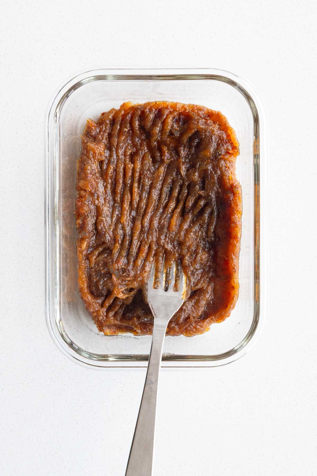 Mashed dates in a glass container with a fork.