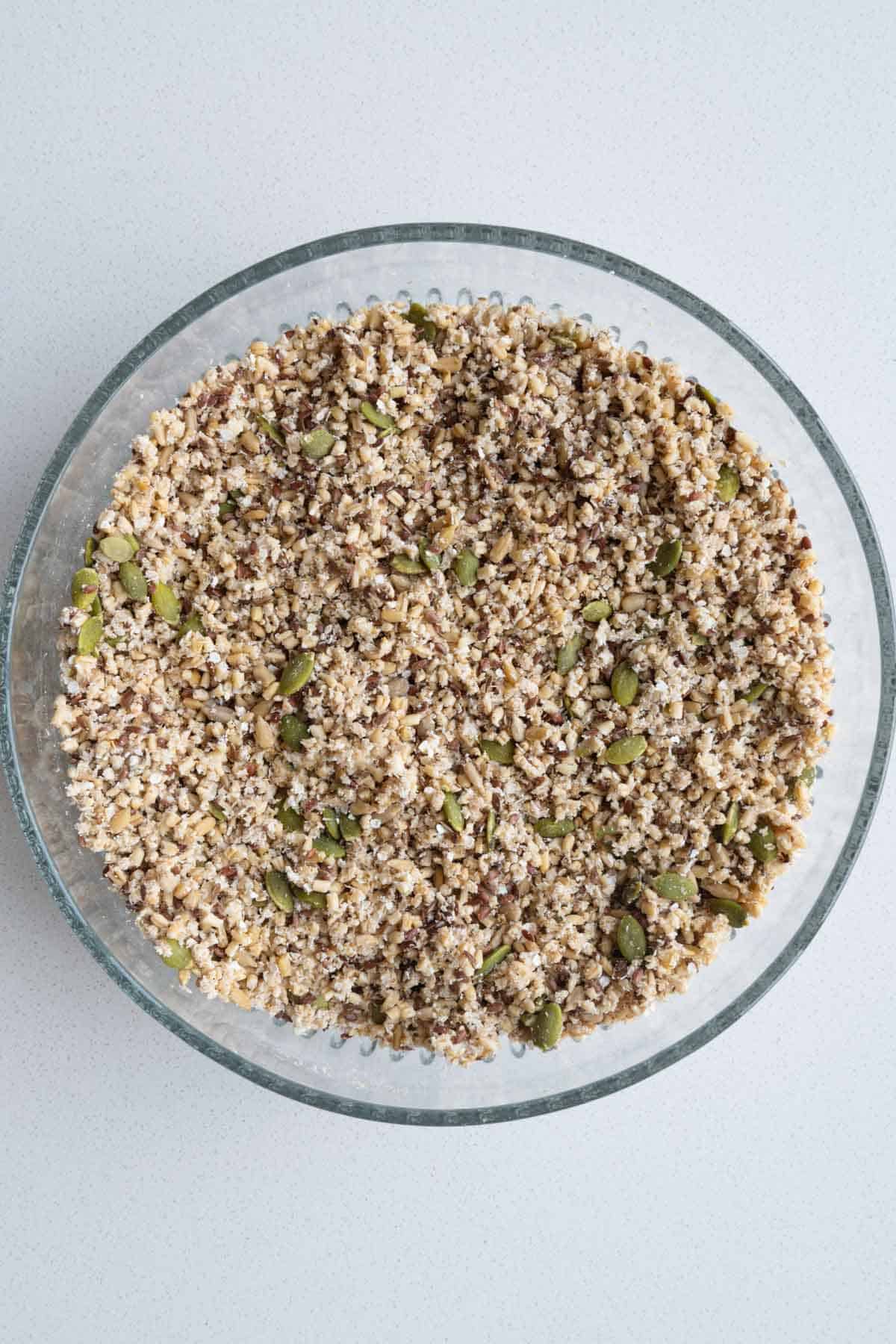 Drained soaked steel cut oats, pumpkin seeds, sunflower seeds, flax seeds, quinoa flakes, and psyllium husks mized in a glass bowl.