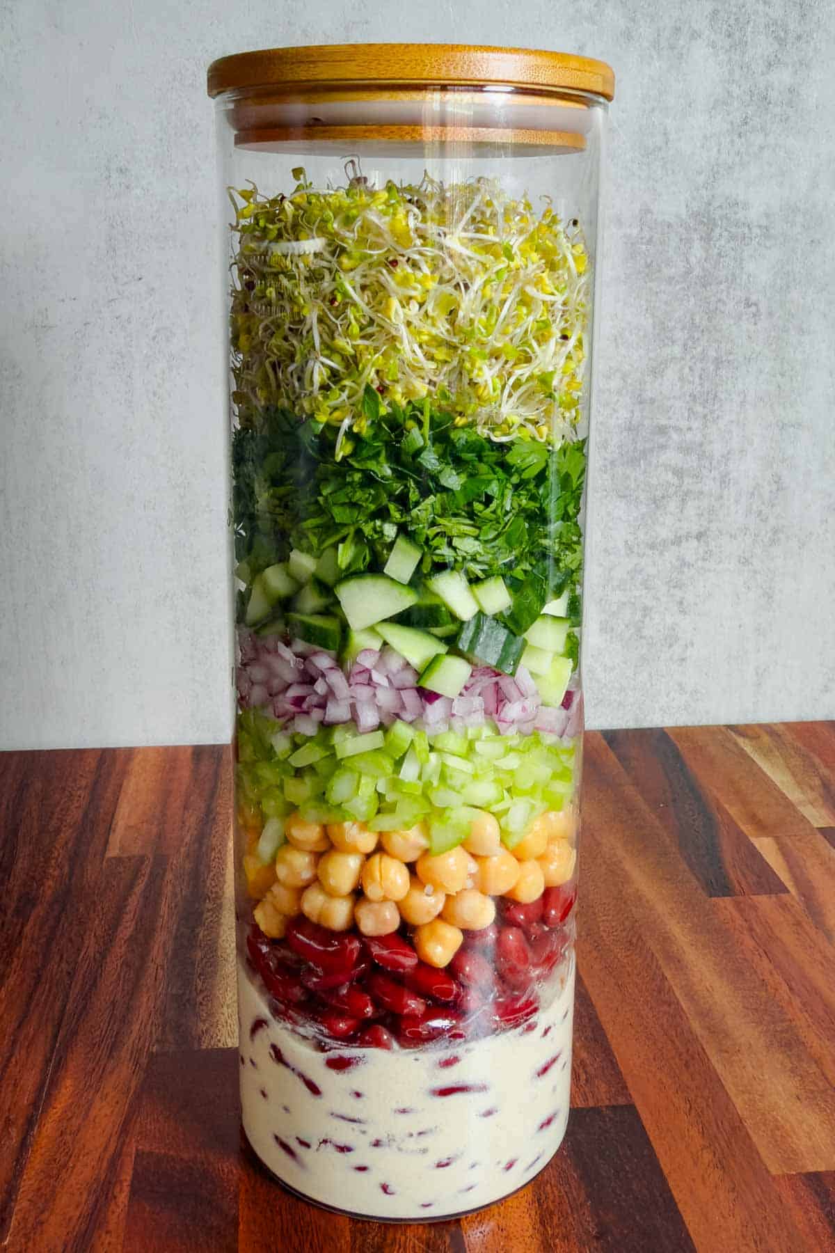 Broccoli sprouts, red onion, cucumber, chickpeas, red kidney beans, parsley, coriander, and creamy lime miso dressing in a salad jar.