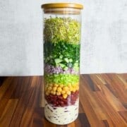 Broccoli sprouts, red onion, cucumber, chickpeas, red kidney beans, parsley, coriander, and creamy lime miso dressing in a salad jar.