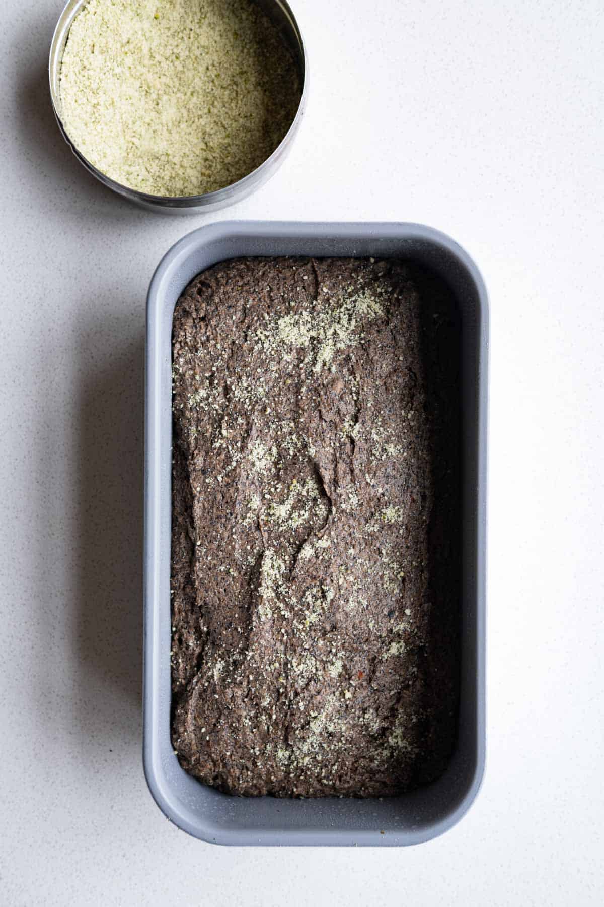 Cake batter in a loaf pan topped with ground pumpkin seeds.