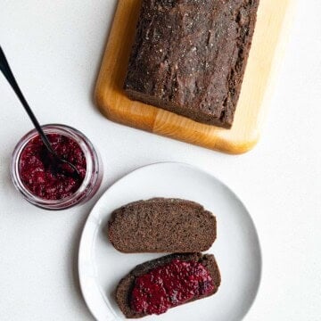 Black sesame cake sliced on a cutting board served on white plate with chia jam.