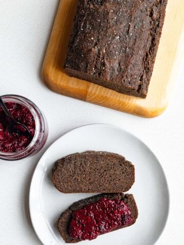 Black sesame cake sliced on a cutting board served on white plate with chia jam.