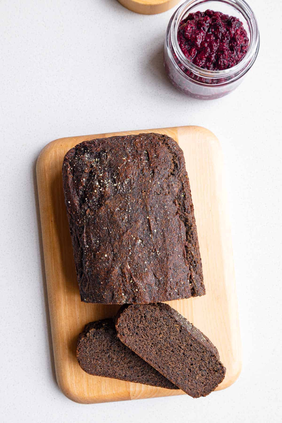 Black sesame cake sliced on a cutting board with chia jam.