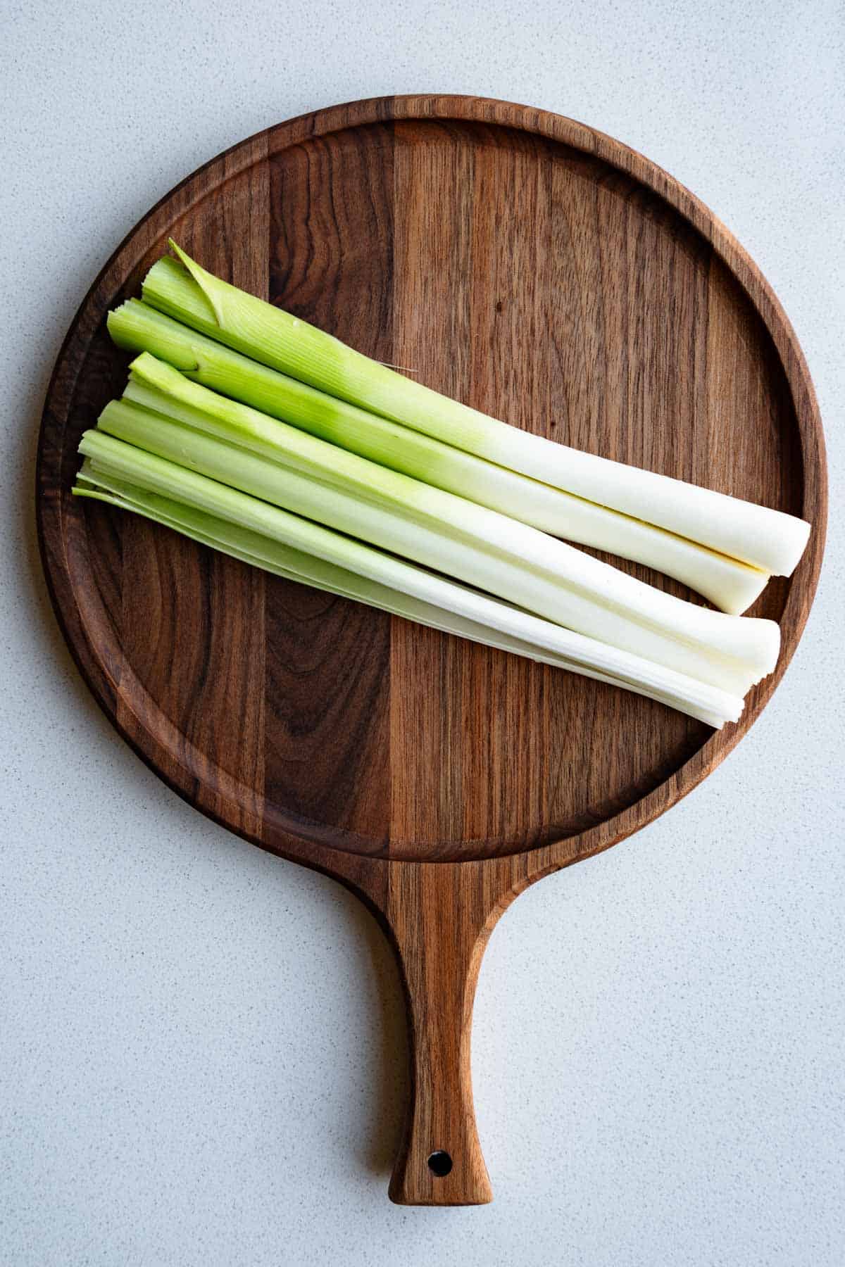 One medium leek, tough dark green parts and root end trimmed, quartered lengthwise on a cutting board.