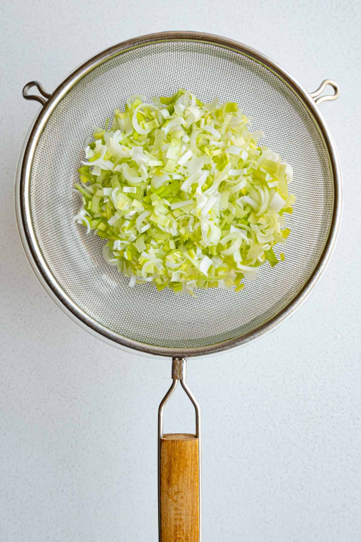 Chopped clean leek in a fine mesh sieve.