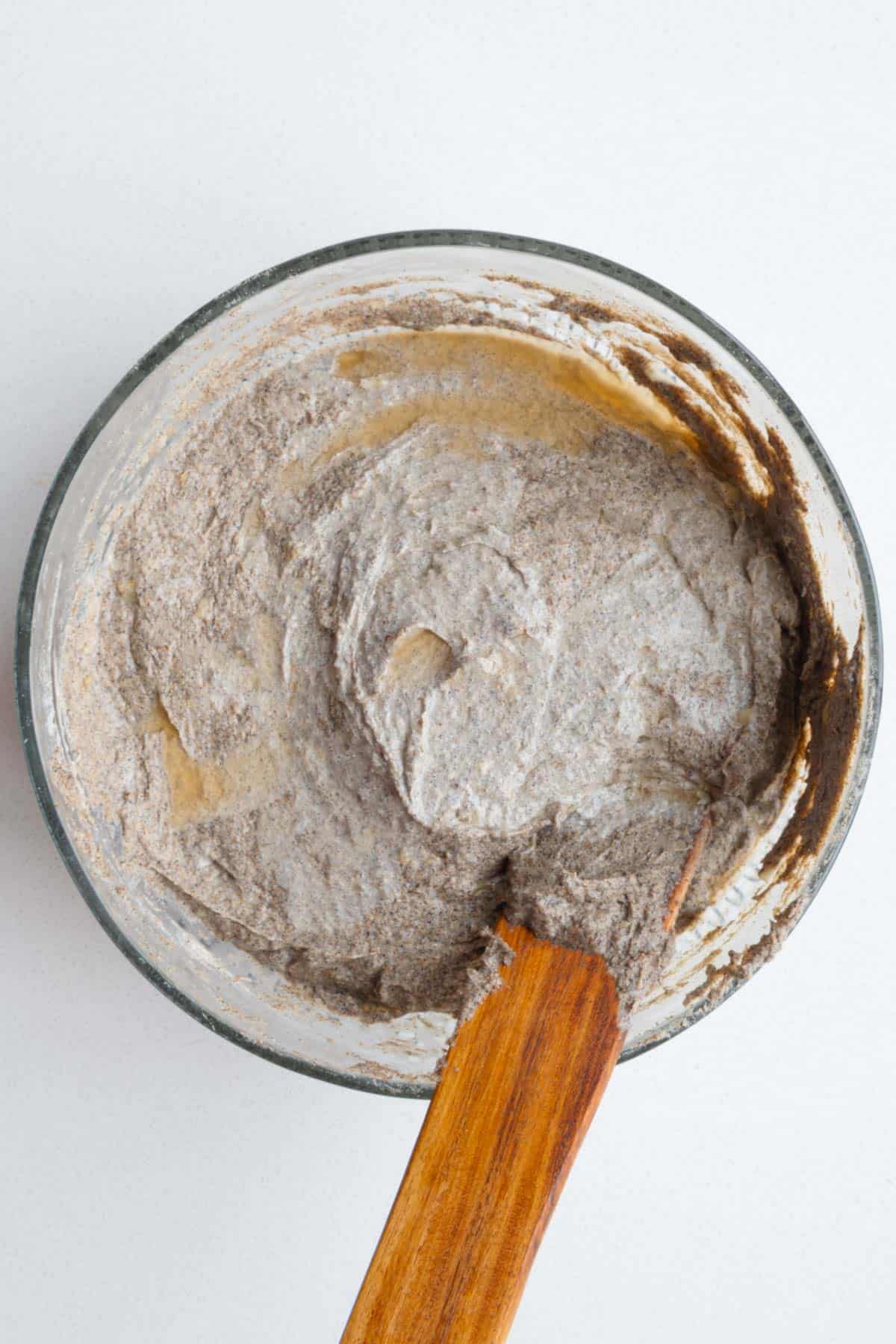 Batter in a glass bowl with apple cider vinegar and a wooden spatula.