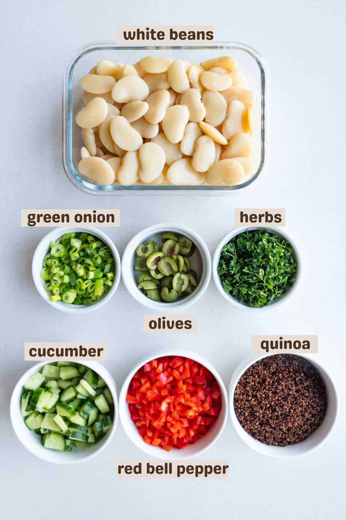 Butter beans, red quinoa, olives, chopped herbs, scallions, cucumber and bell pepper with pumpkin seed dressing in a meal prep container.