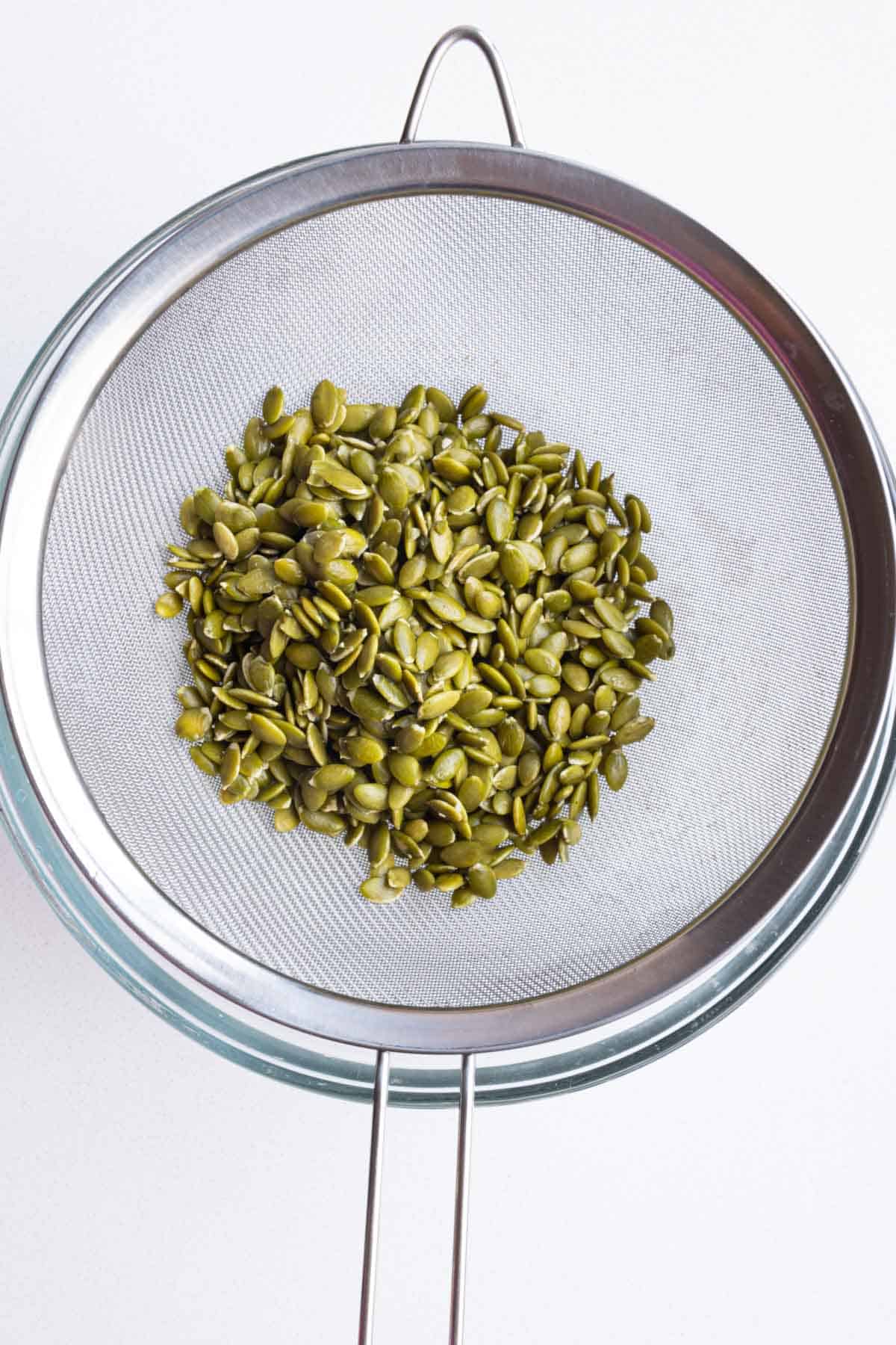 Drained soaked pumpkin seeds in a fine mesh sieve.