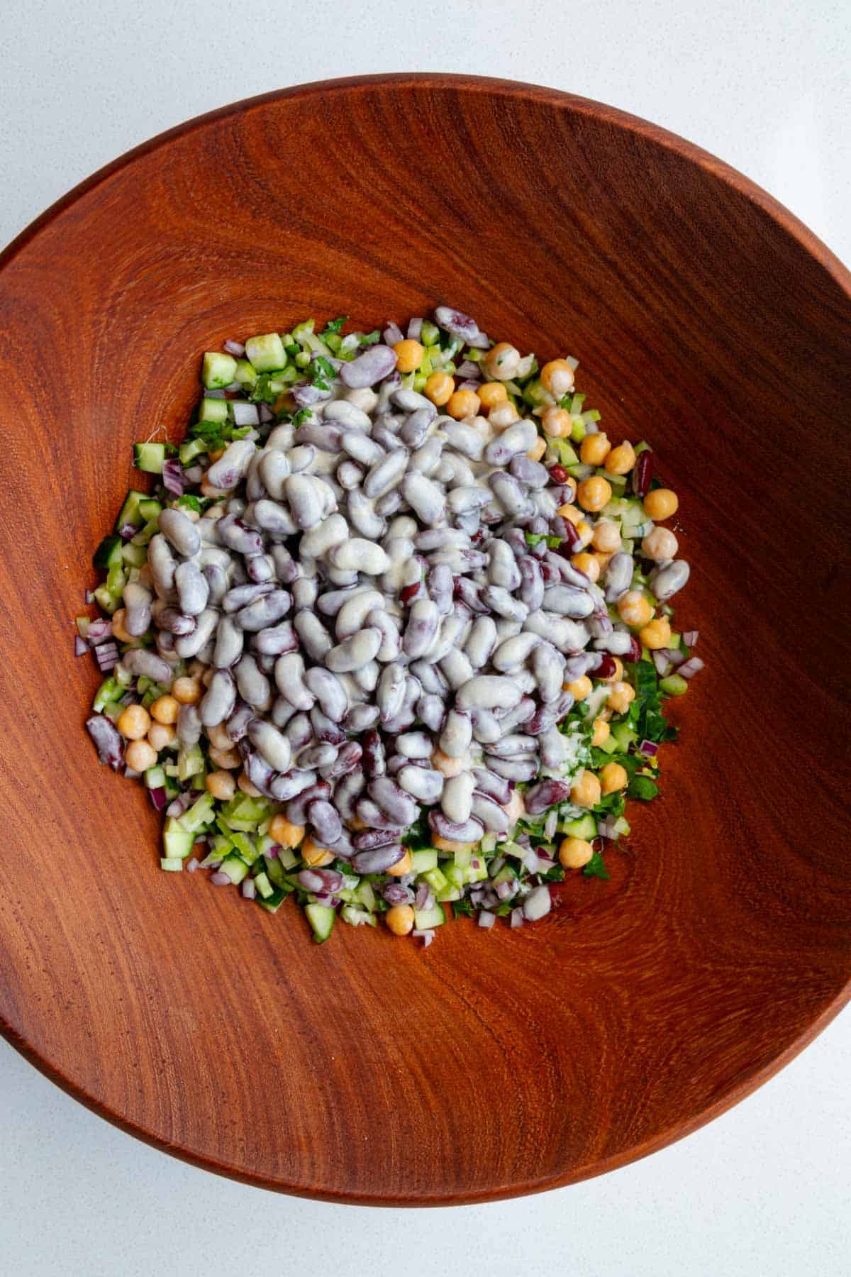 Broccoli sprouts, red onion, cucumber, chickpeas, red kidney beans, parsley, coriander, and creamy lime miso dressing in a wooden bowl.
