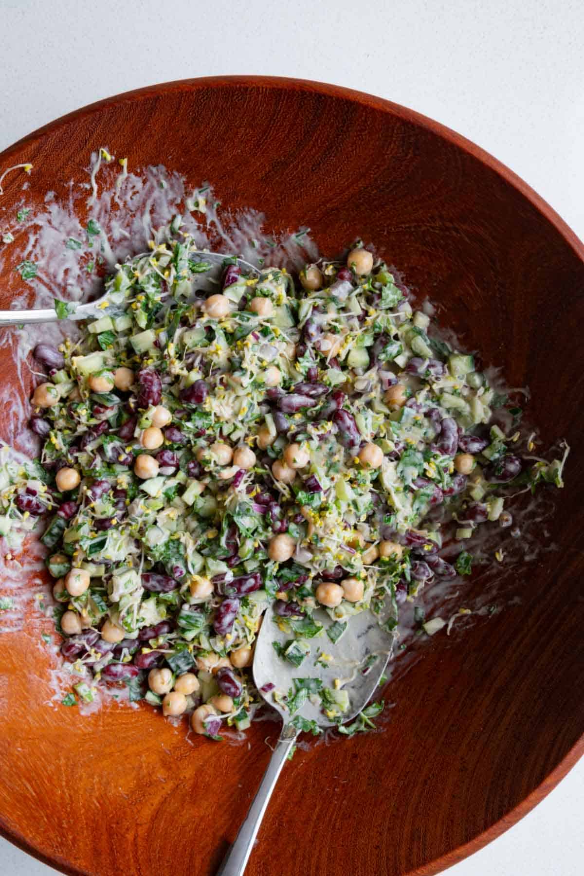 Broccoli sprouts, red onion, cucumber, chickpeas, red kidney beans, parsley, coriander, and creamy lime miso dressing in a wooden bowl.