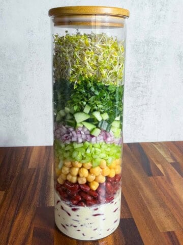 Broccoli sprouts, red onion, cucumber, chickpeas, red kidney beans, parsley, coriander, and creamy lime miso dressing in a salad jar.