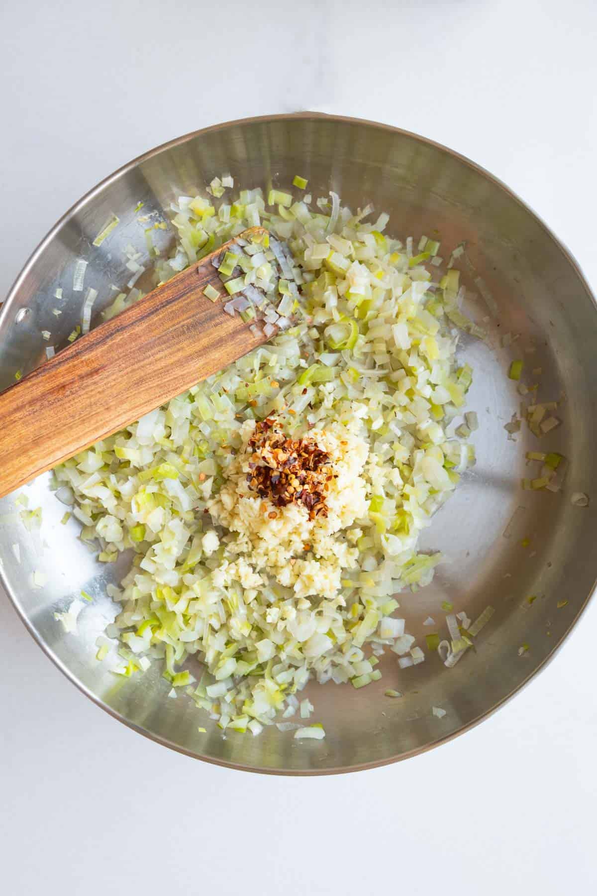 Cooked leek and onion with chopped garlic and crushed red pepper in a large stainless skillet.