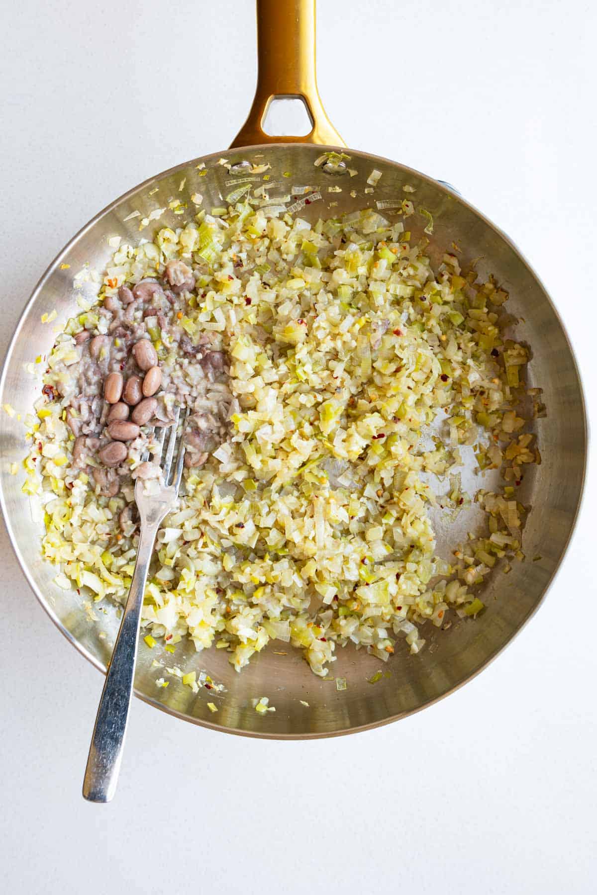 Cooked aromatics in a saucepan with beans.