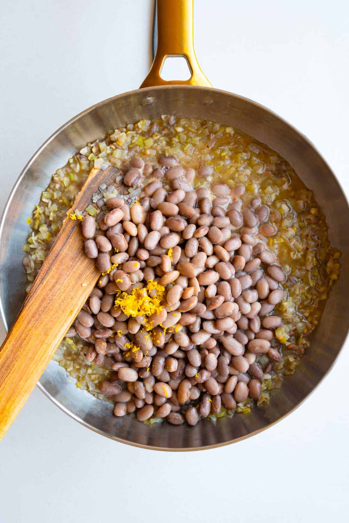 Cooked leek and onion with beans, lemon zest, and broth in a saucepan.