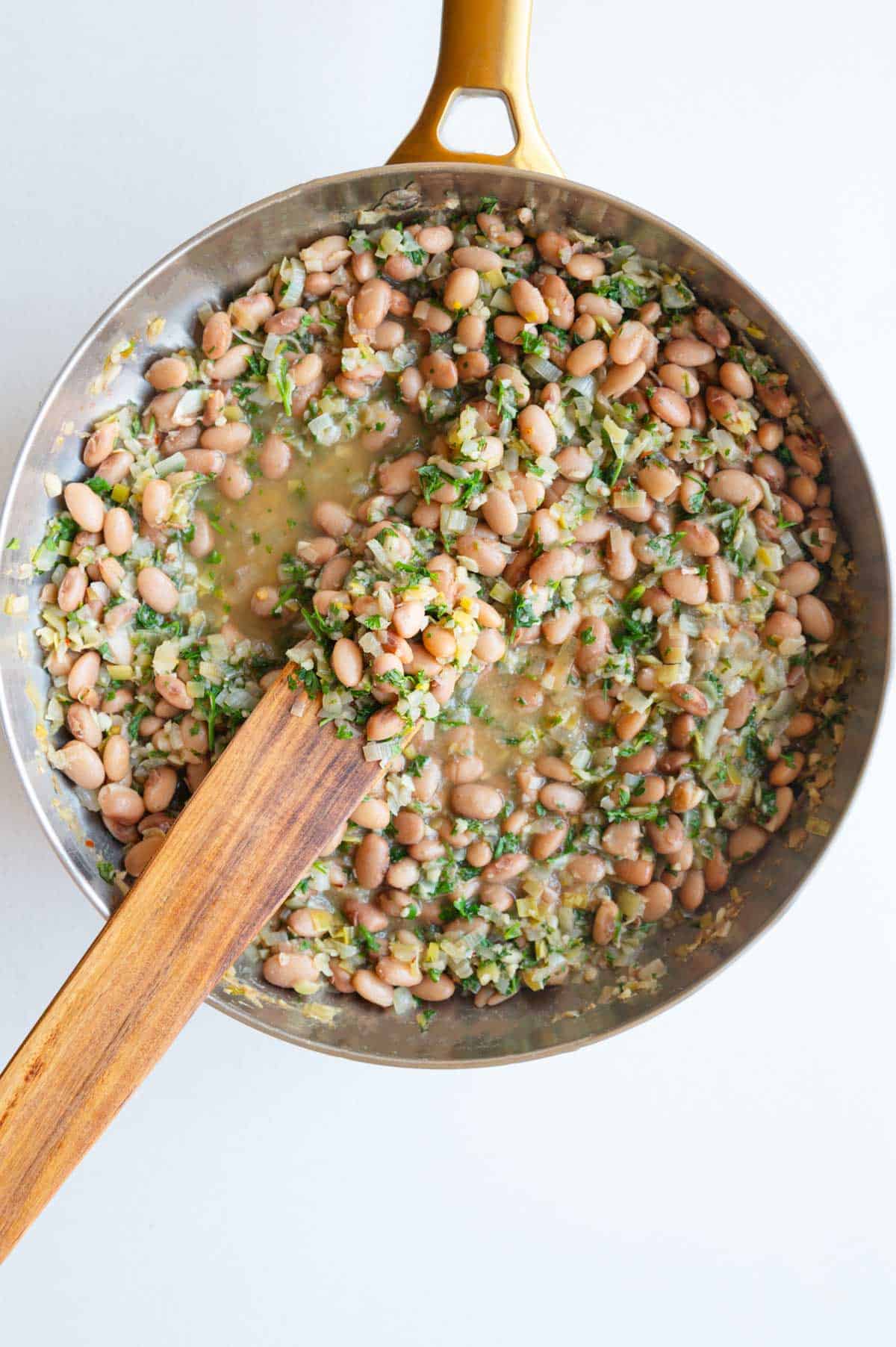 Brothy pinto beans with lemon, leeks, and fresh herbs in a saucepan.