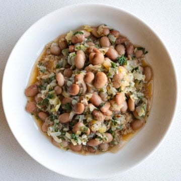 Brothy vegan beans with lemon, leeks, and fresh herbs in a bowl.