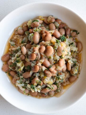 Brothy vegan beans with lemon, leeks, and fresh herbs in a bowl.